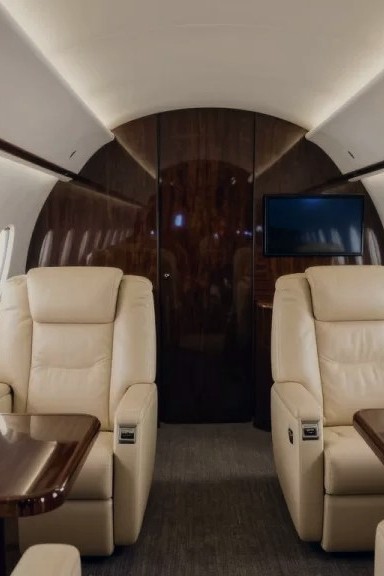 Cabin interior with cream leather club seats, polished wood tables, and oval windows
