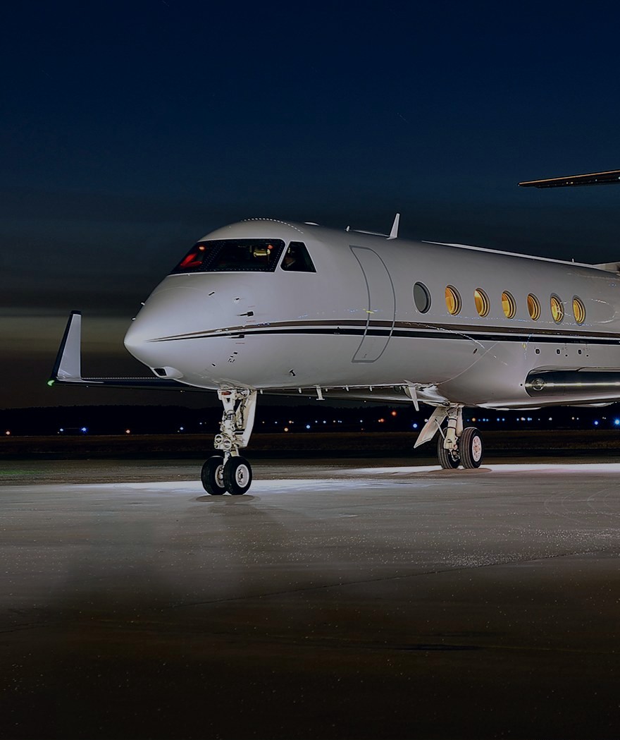 Business jet nose and cockpit on the ramp at dusk, cabin windows lit