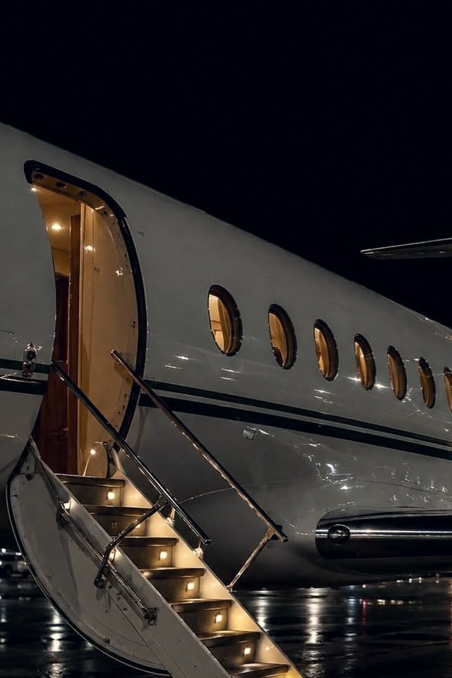 Business jet at night with its airstair down and cabin glowing, reflected on a wet ramp